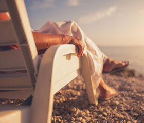 Persona tomando el sol y viendo el atardecer sentada en una silla en la playa